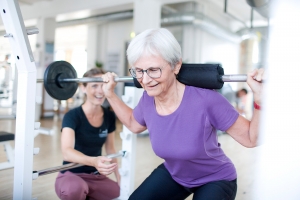 Ældre kvinde der squatter med vægte hos fysisk form